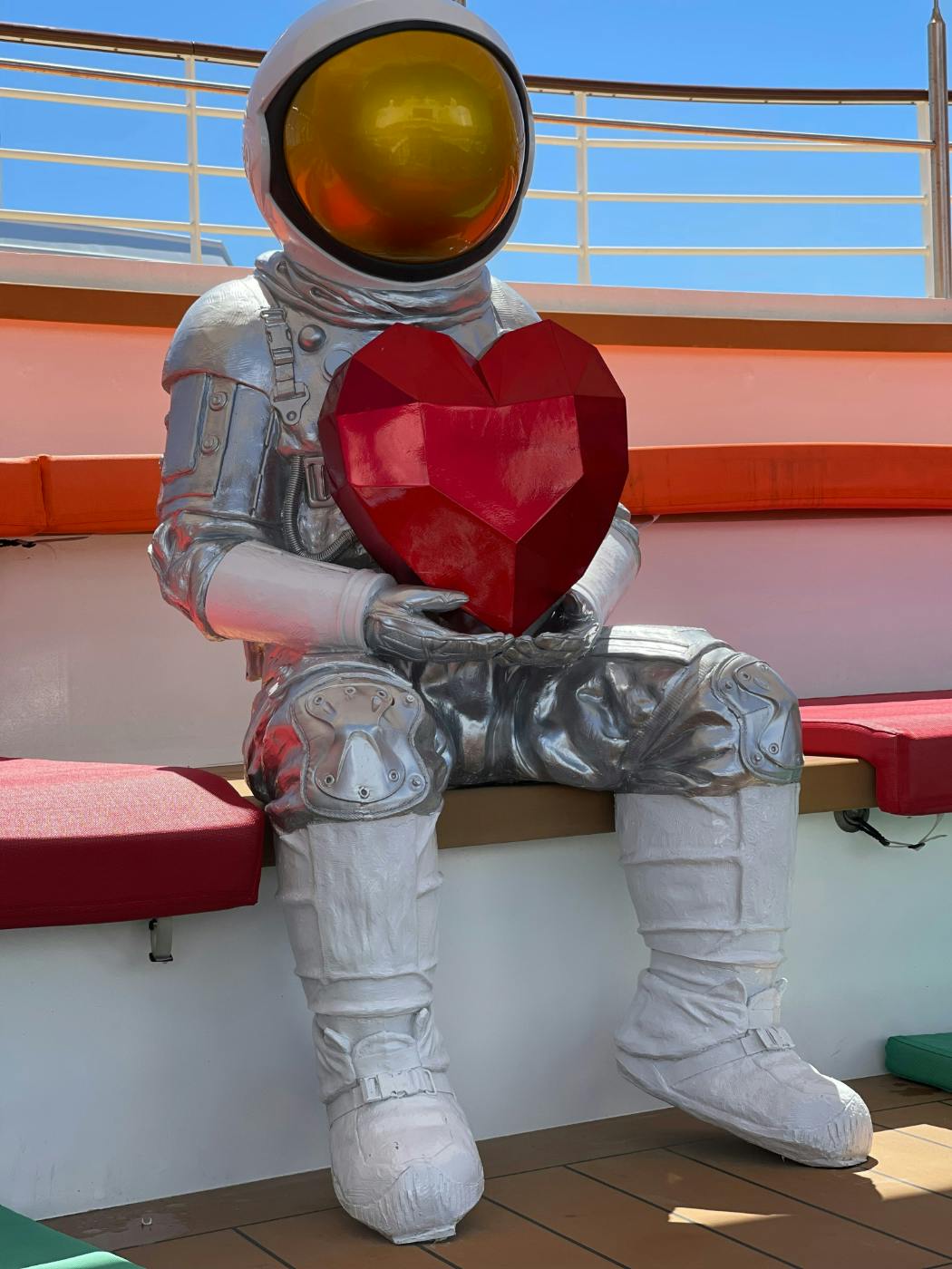 A Statue of an Astronaut sitting on bench holding a heart shaped red object