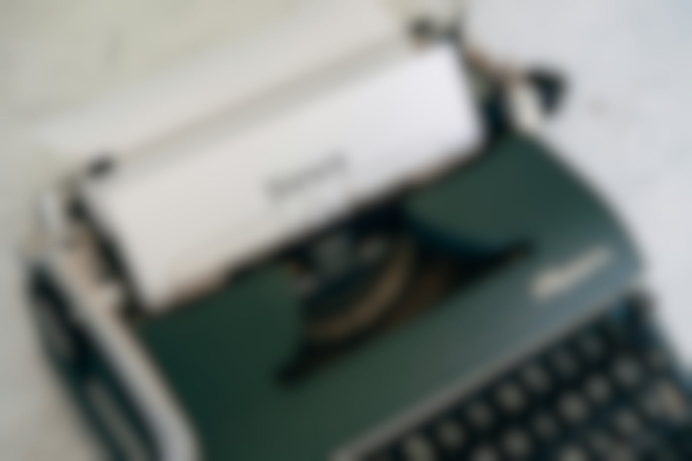 A green Olympia typewriter with a sheet of paper in the roller with NEWS typed on it.