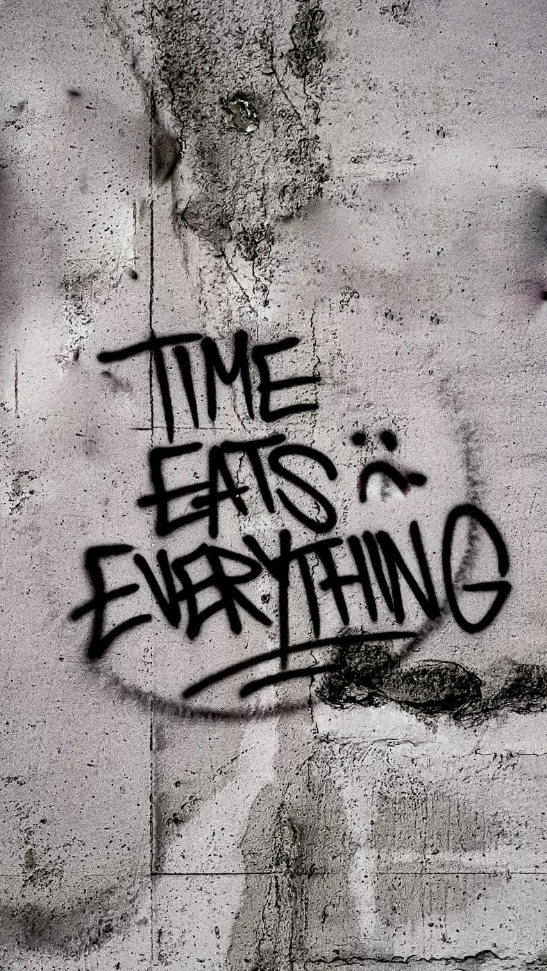 Black graffiti on a gray wall reading: Time Eats Everything
