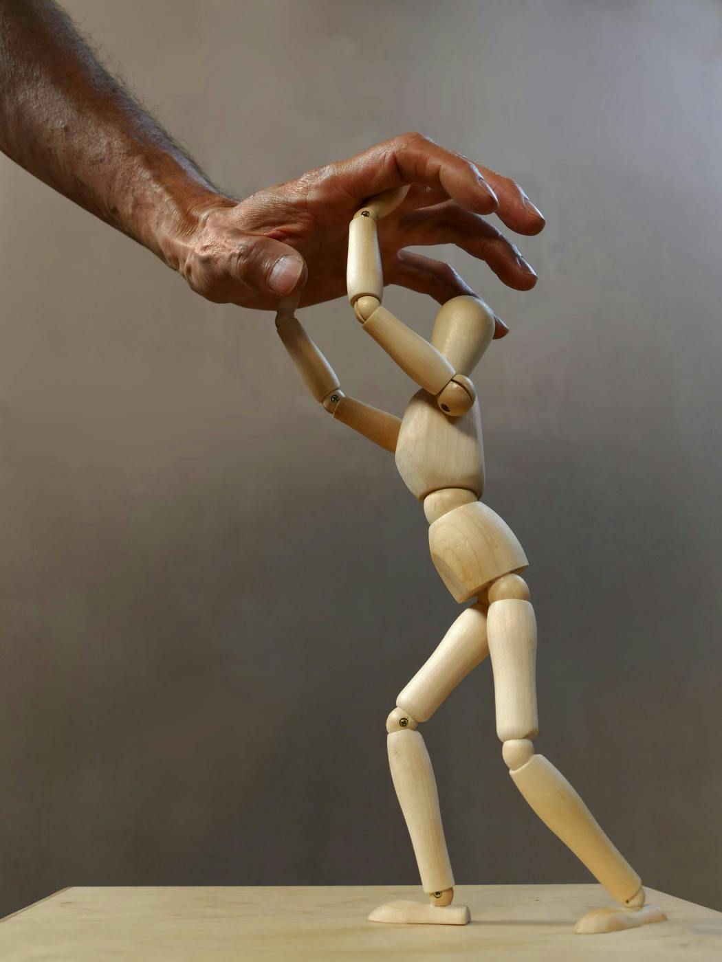 A small artist's mannequin fighting off a human hand