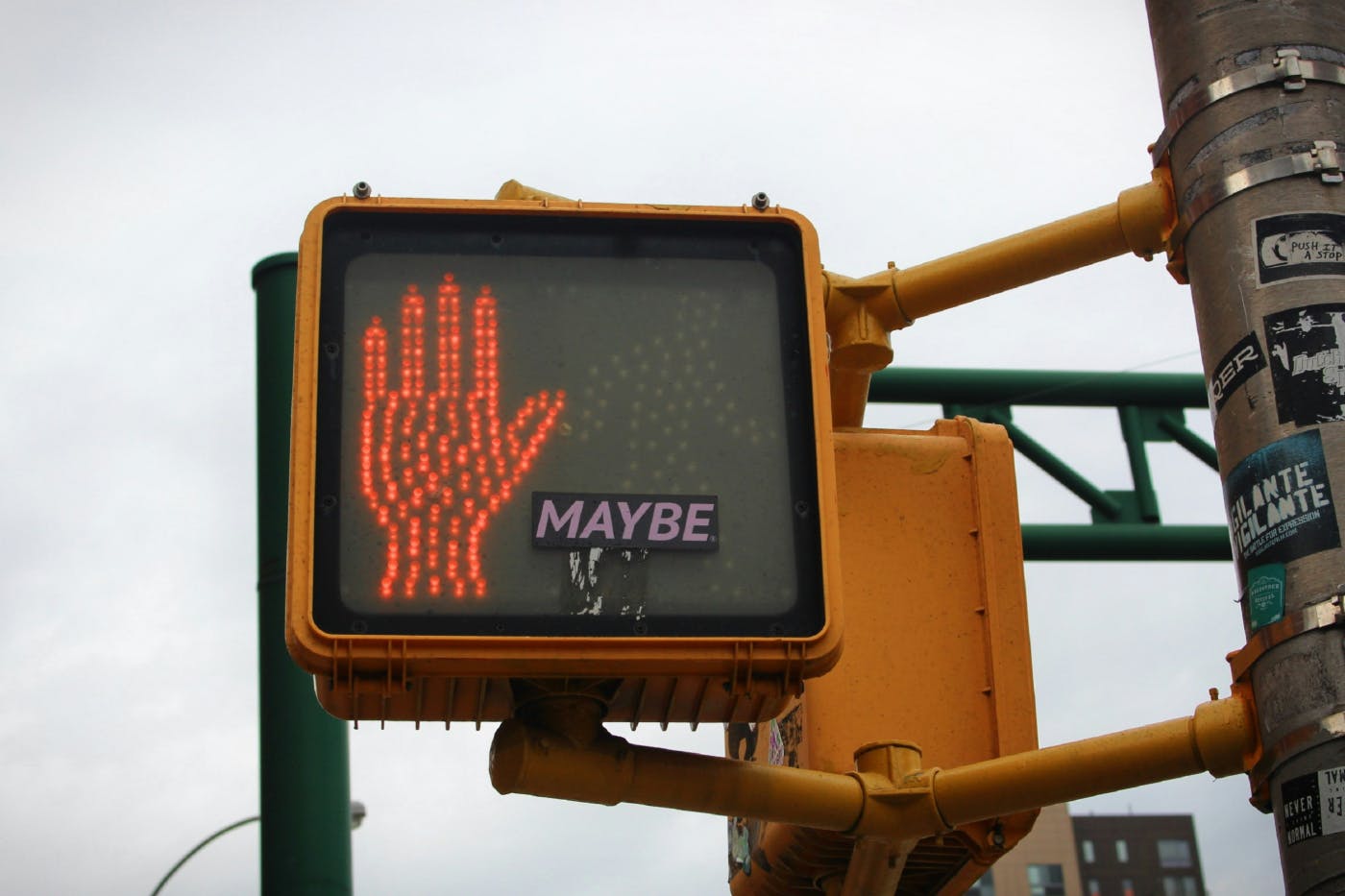 The red stop hand of a traffic light with a small sticker reading 'maybe' next to it