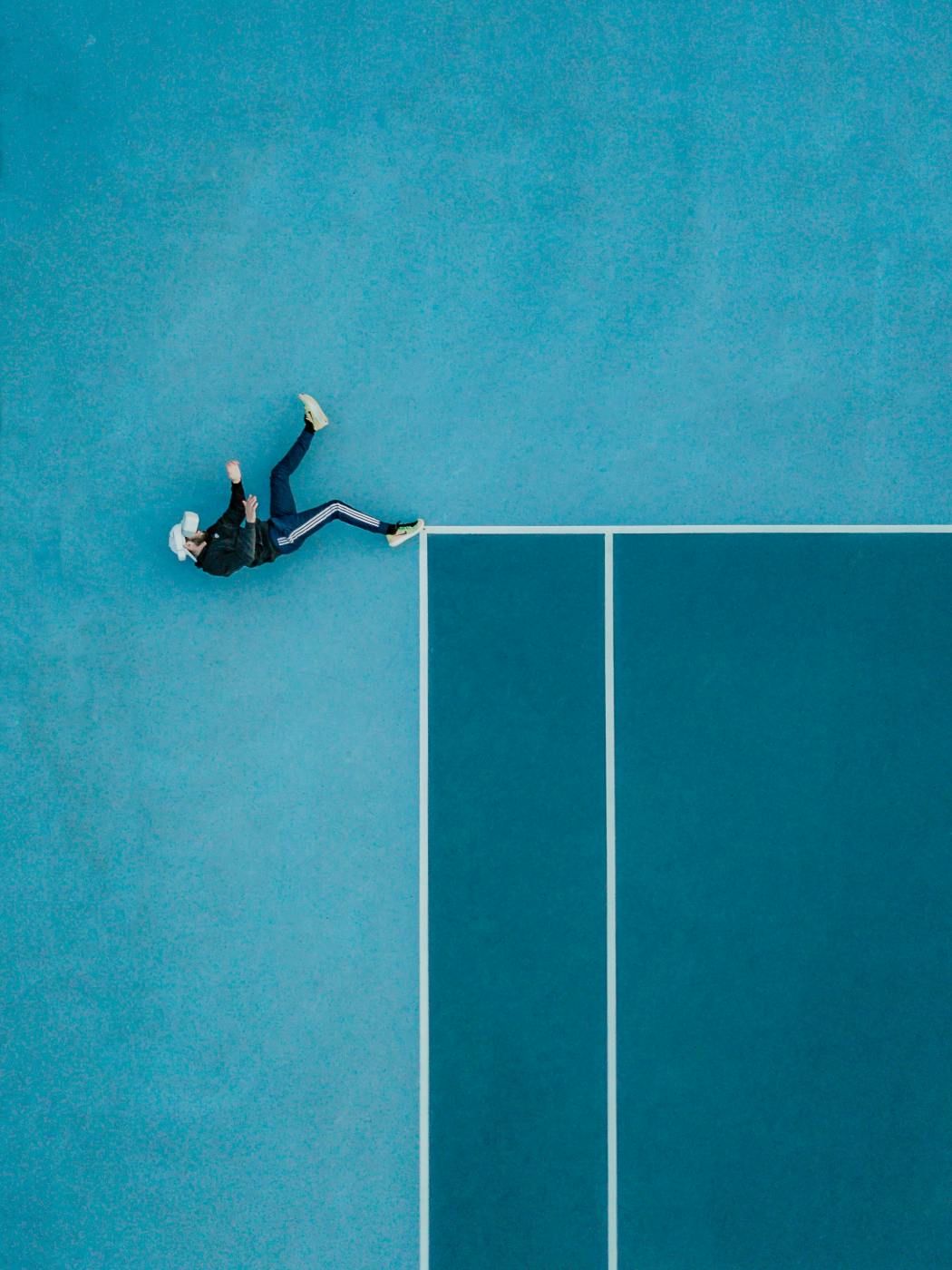 A man in a black track suit wearing a VR goggles, laying on a tennis court