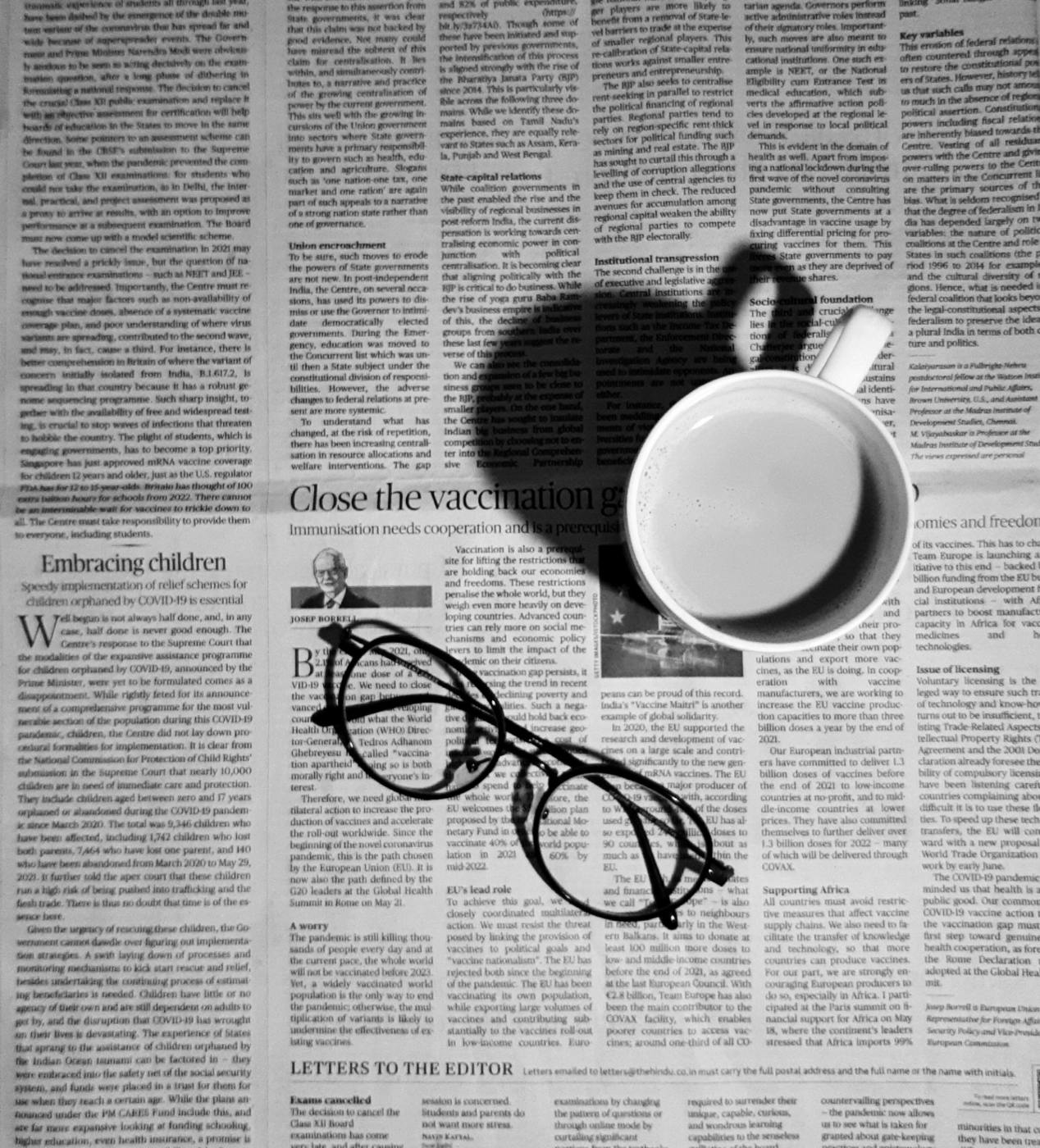 A cup of coffee and a pair of glasses sitting on a page of newspaper