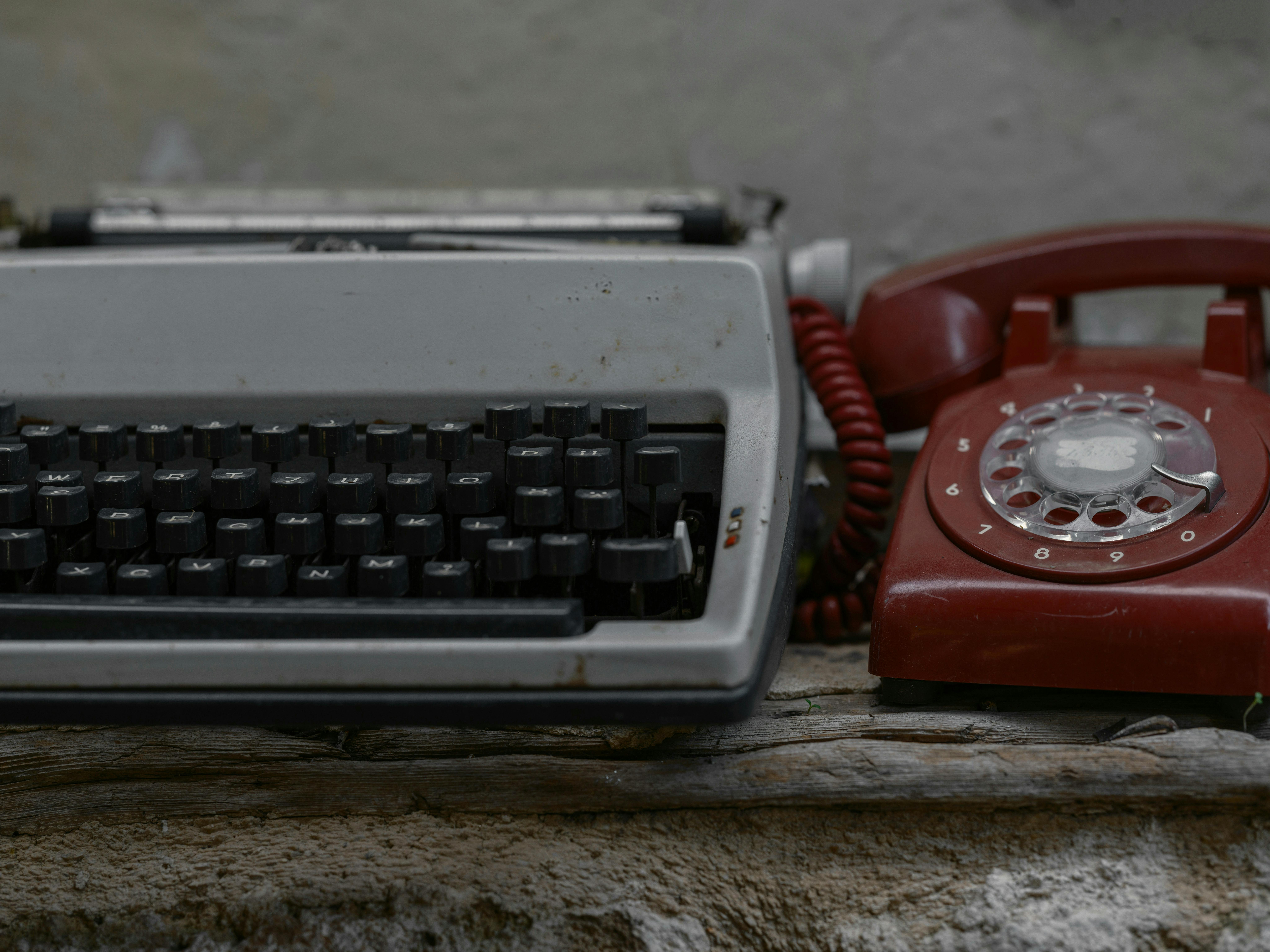An old typewriter and a red old fashioned telephone sitting on a table
