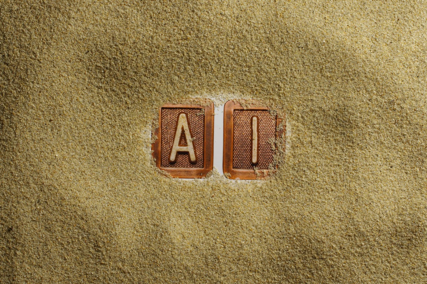 The letters A & I in wood tiles surrounded by sand