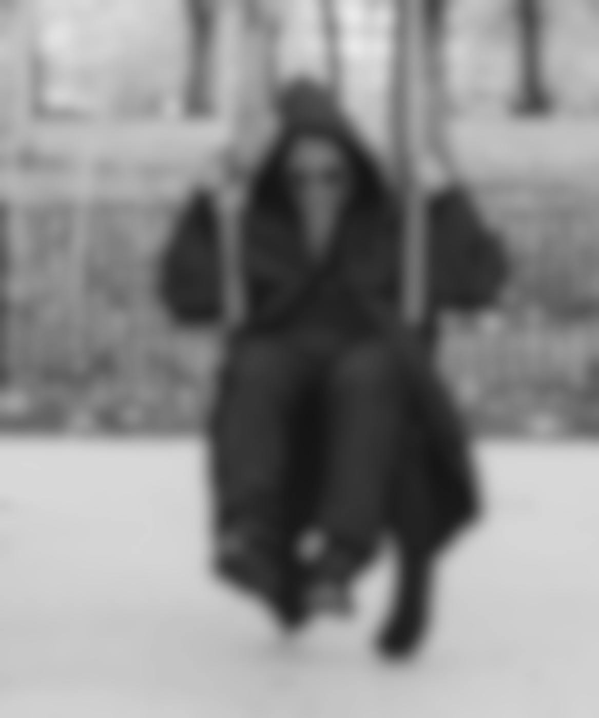 A personal all in black wearing a a plague mask on a swing