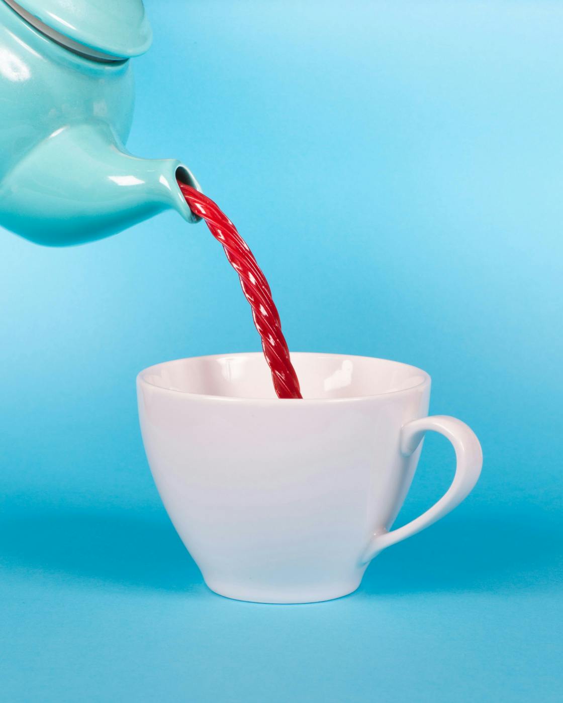 A blue tea pot pouring a red Twizzler into a white cup