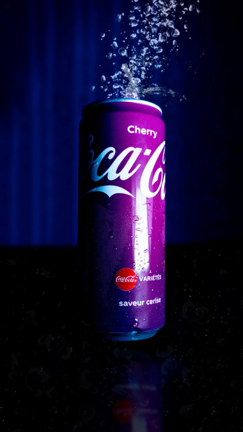 A purple Cherry Coke can with spray coming out of the top