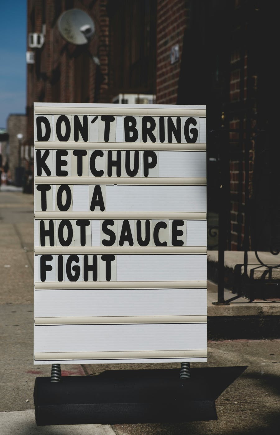 A street sign reading: Don't Bring Ketchup to a Hot Sauce Fight