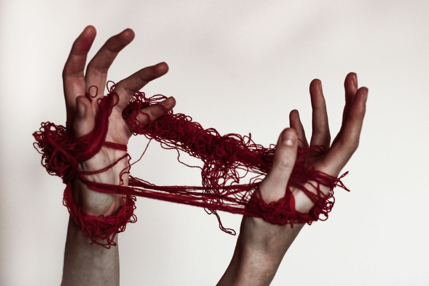 A pair of hands entwined in red thread