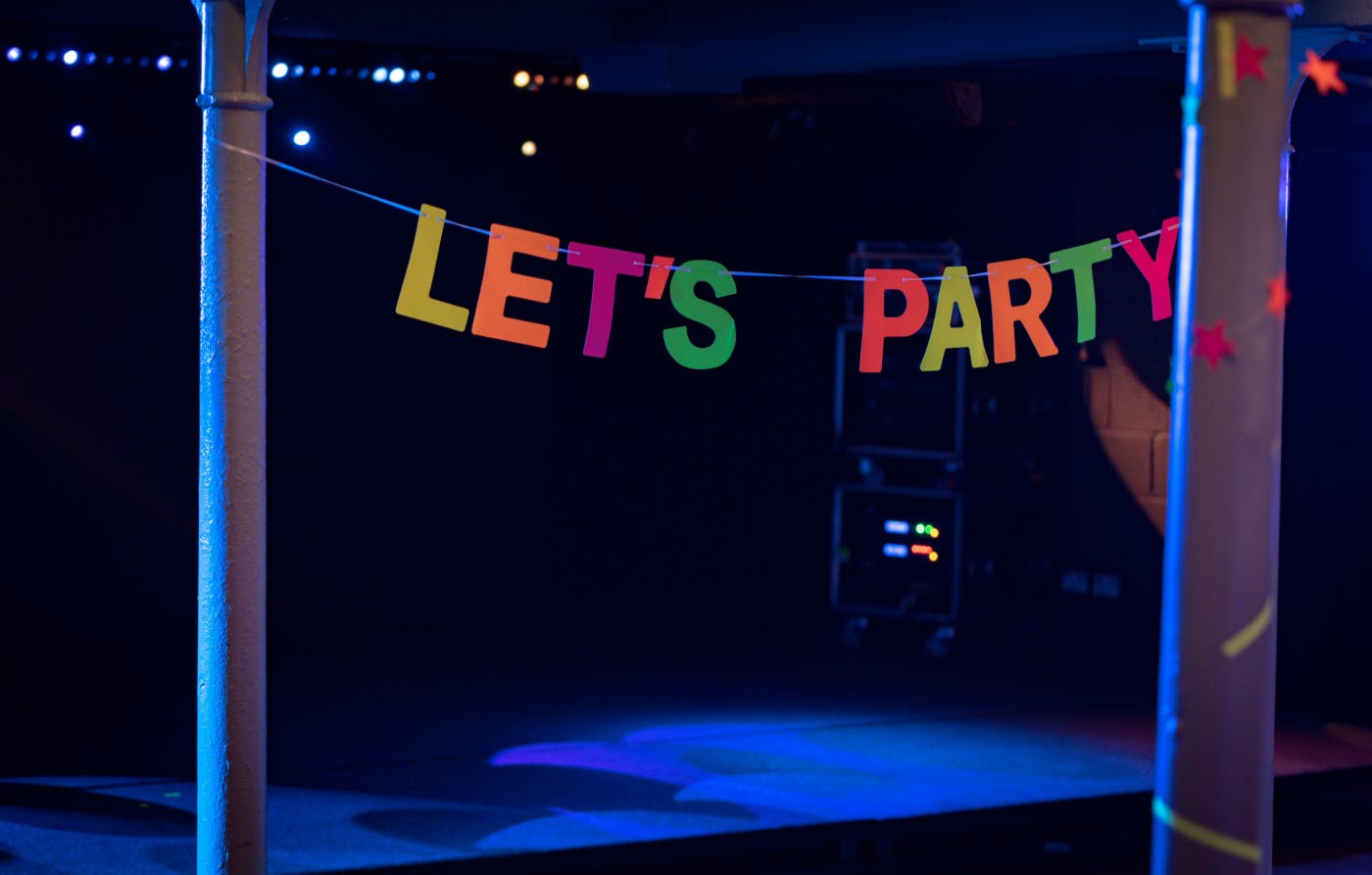 A dimly lit dance floor with a banner reading Let's Party