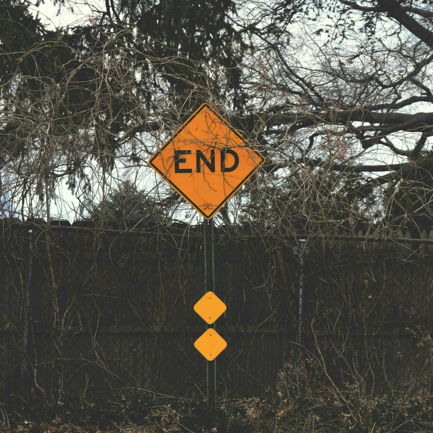 A yellow sign reading END in front of a fence and some shrubs