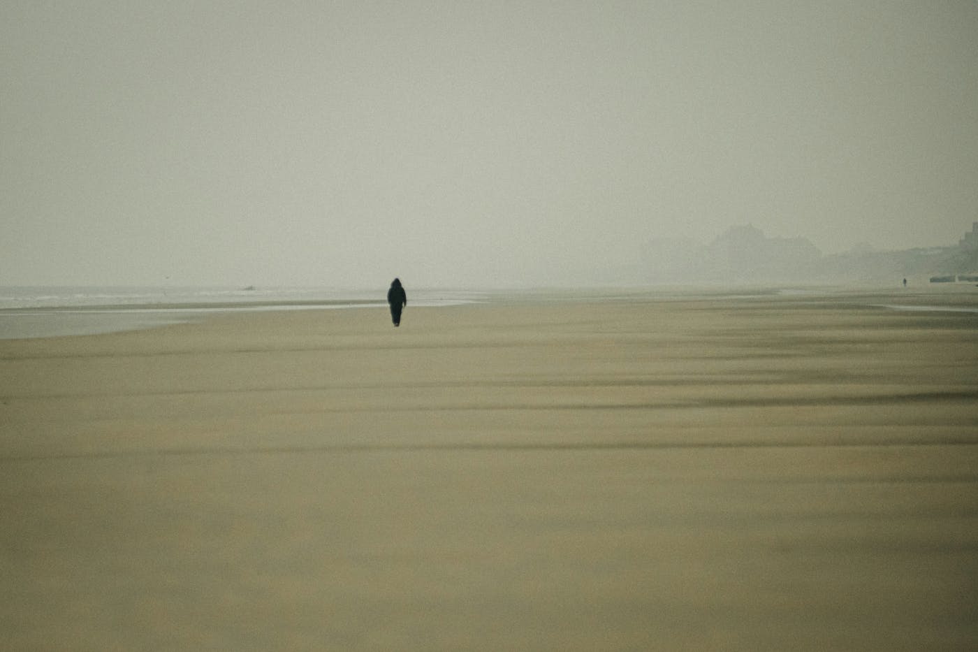 A lone person walking along an empty foggy beach
