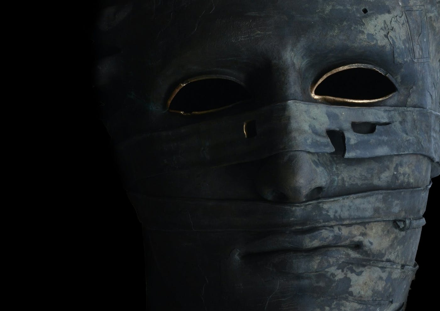 A grey mummy mask with gold painted around the eye holes