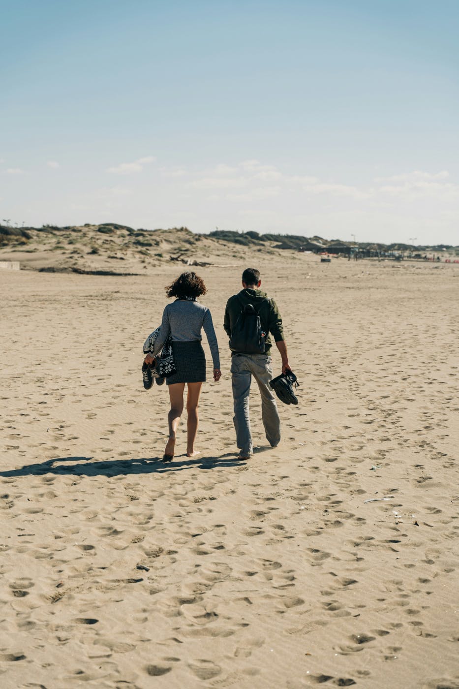 A man and a woman walking barefoot on a beach