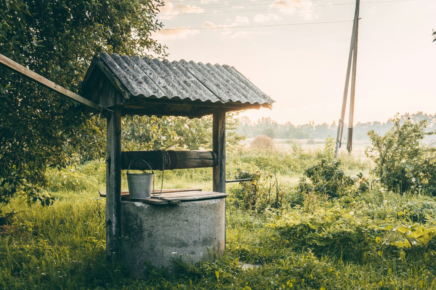 A well with  a little roof and a silver bucket in a field