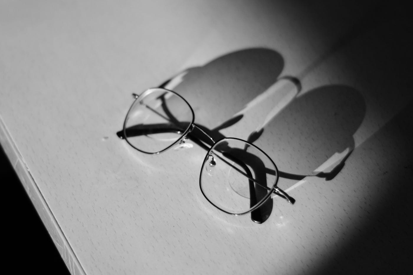 A pair of glasses on a table with a long shadow