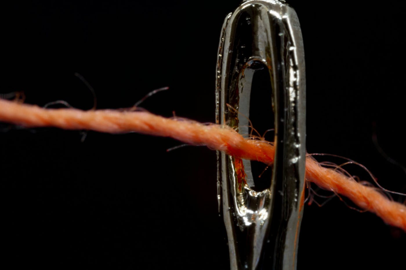 Close up of orange thread passing through the eye of a needle