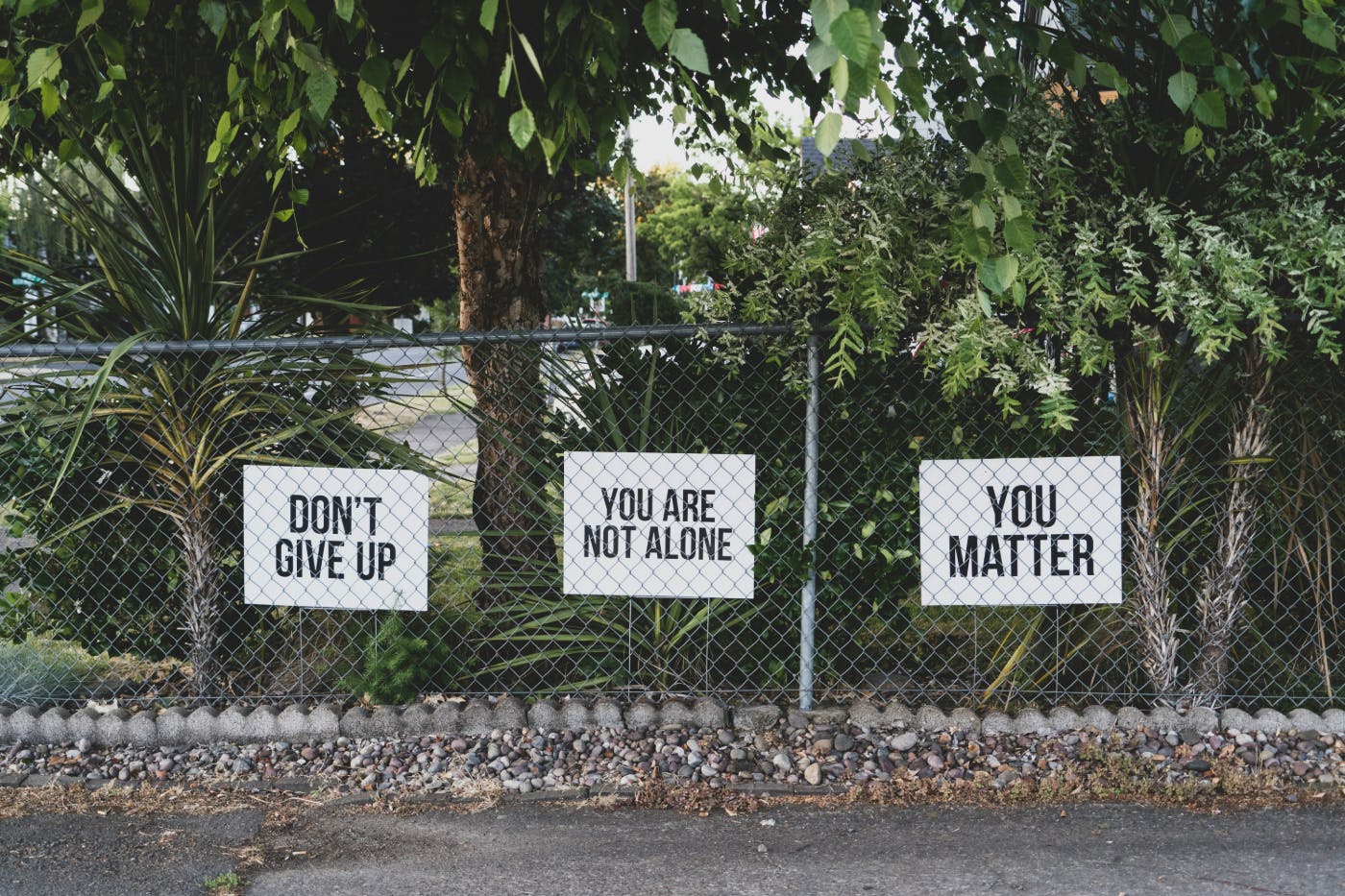 A chain link fence with three signs: Don't Give Up, You Are Not Alone and You Matter