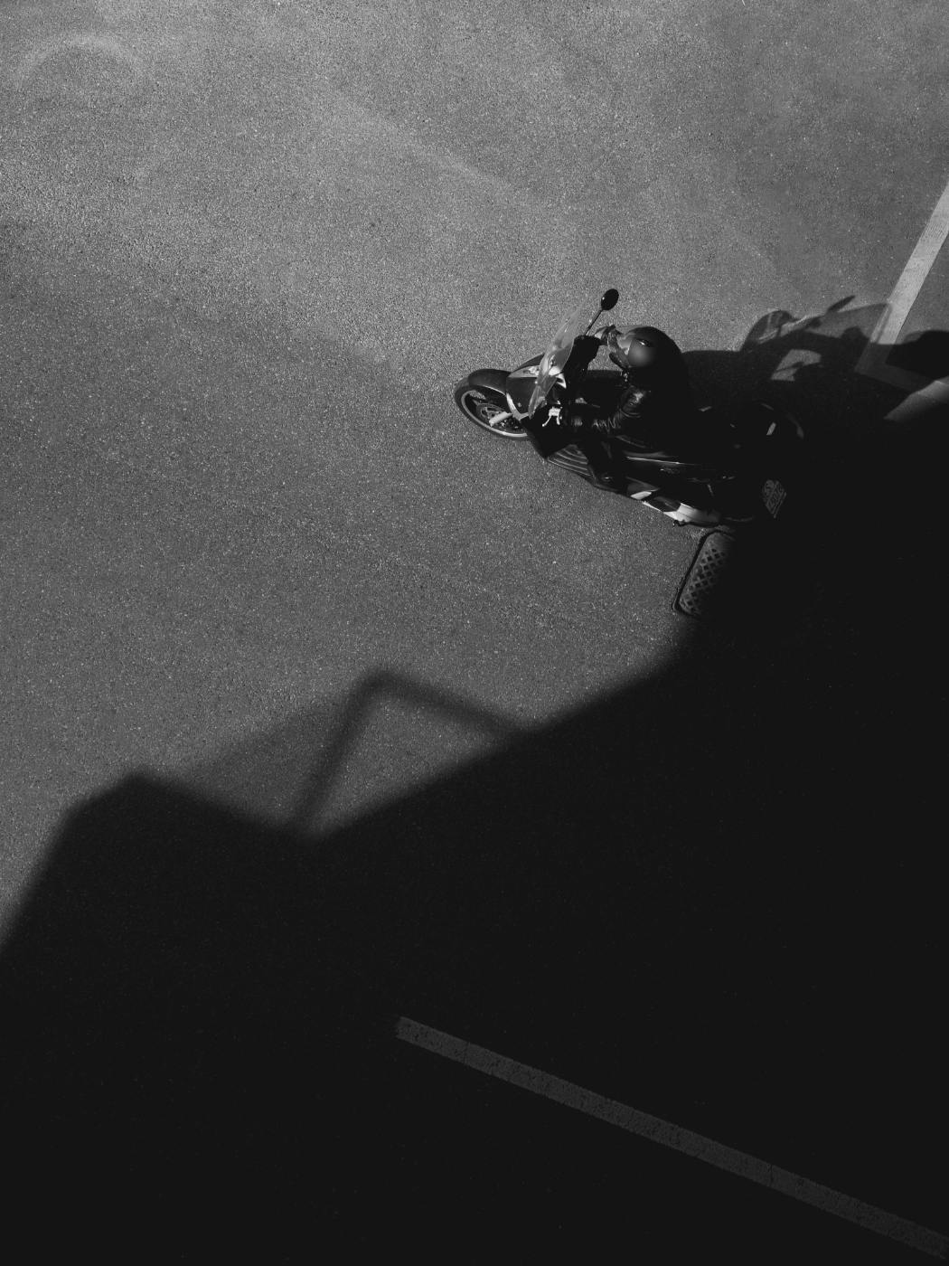A person on a motorcycle driving out of the shadows