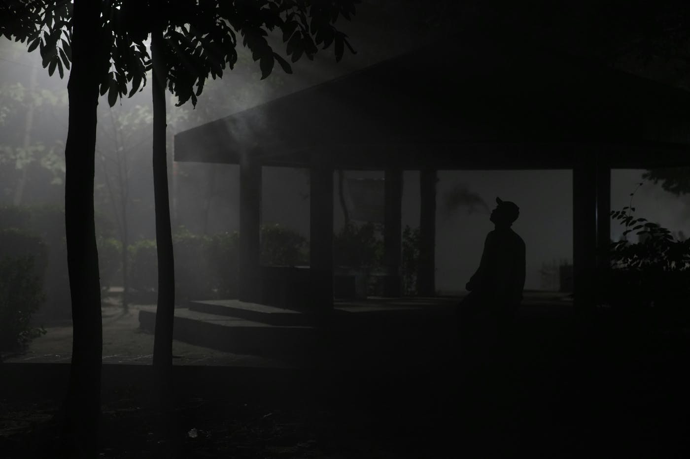 A man in a baseball hat standing in the dark shadows