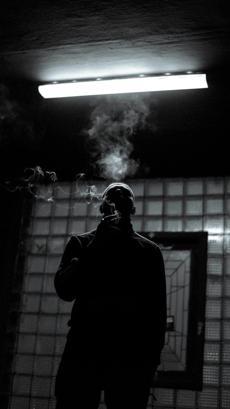 Black and white of a man under florescent light smoking