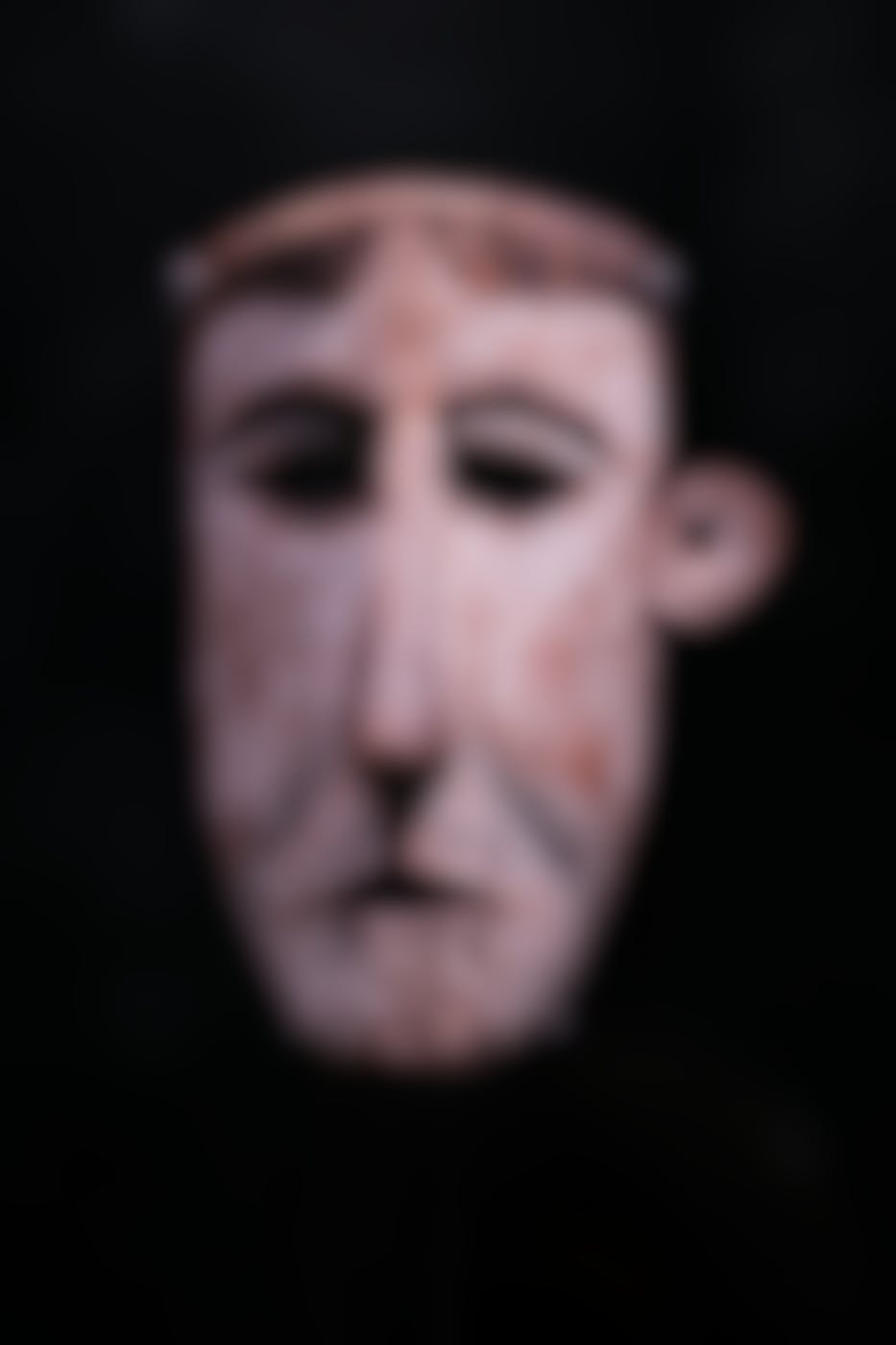A tribal mask of a man on a black backdrop