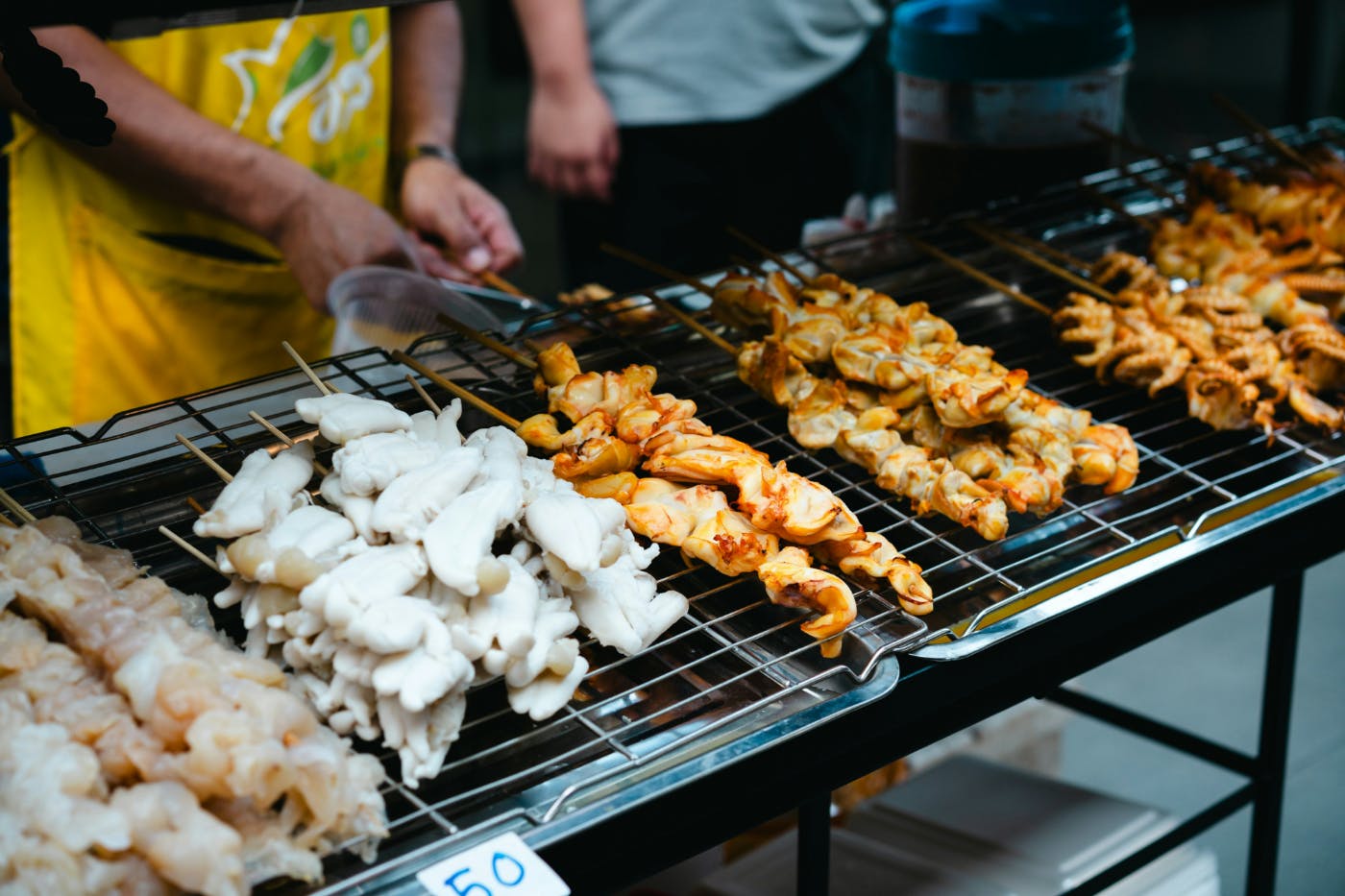A variety of meats on skewers being grilled at an outdoor market
