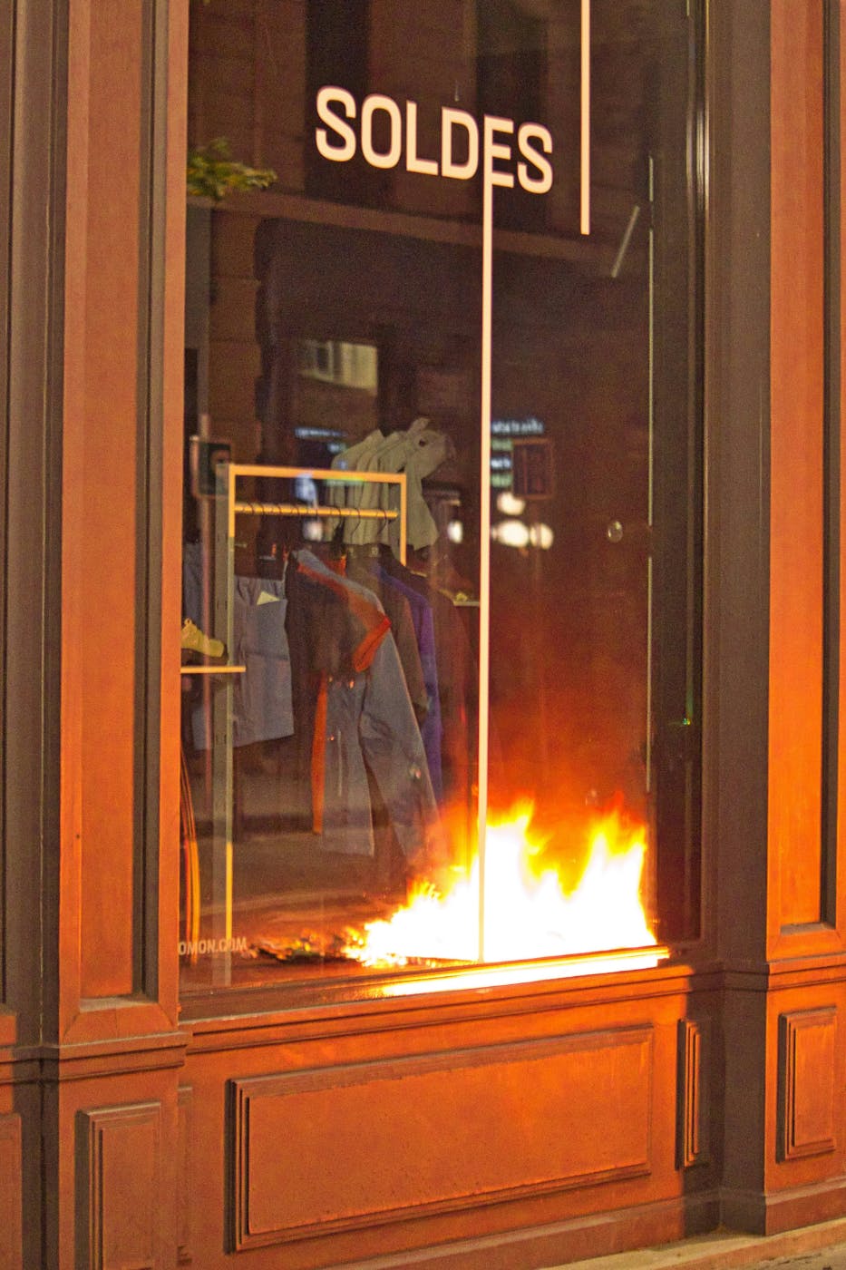 Looking in the window of a French clothing shop, with Soldes (Sale) on the window and the refection of a fire