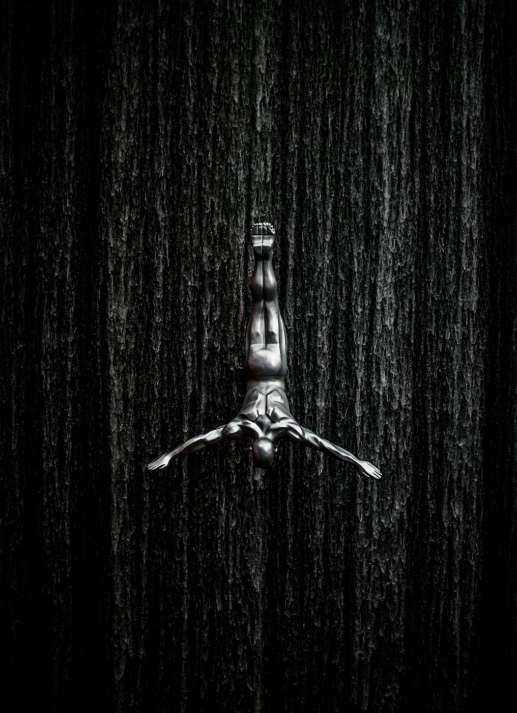 Gray scale of a statue of a man diving in front of a waterfall