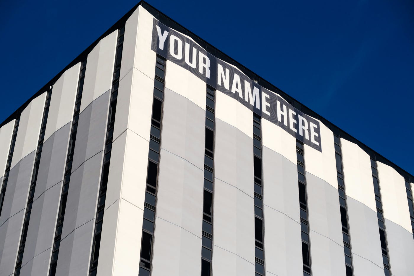 The side of a gray and white building with a banner at the top reading: YOUR NAME HERE