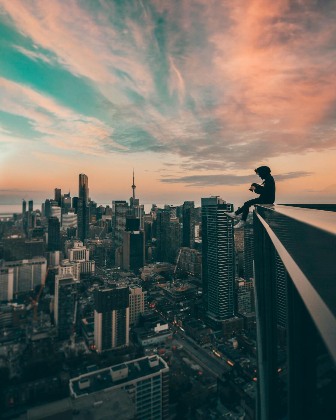 A person sitting on the ledge of a building looking out over a city