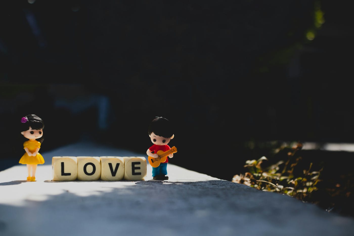 A toy girl and a toy boy with a guitar standing on either side of the word love spelled out in blocks