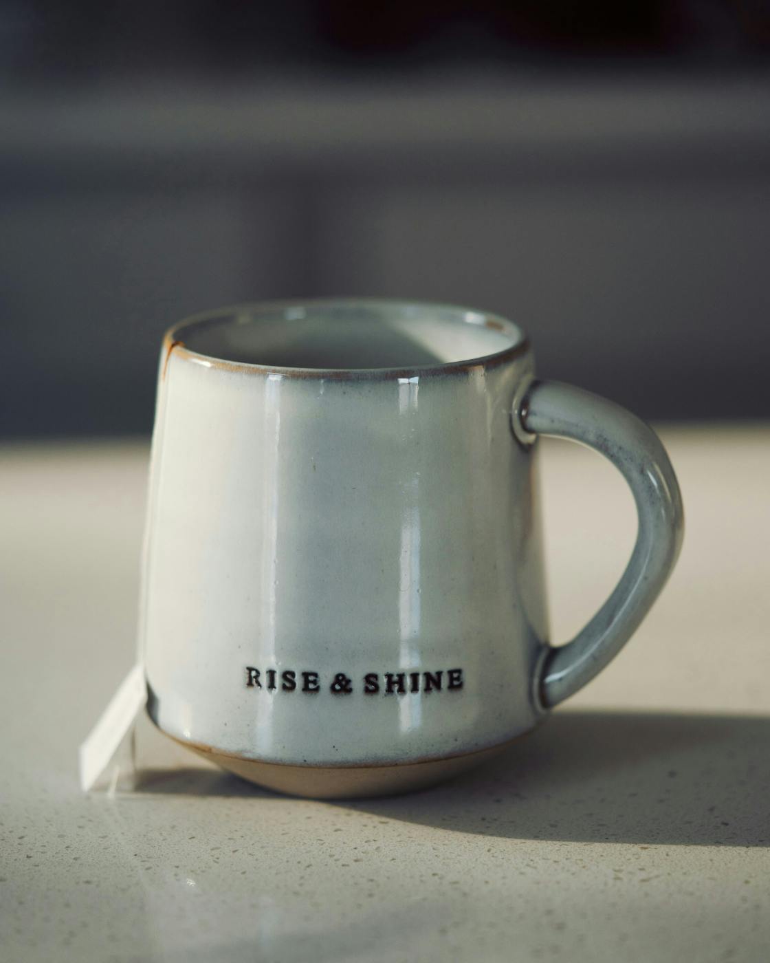 A gray coffee mug with rise & shine on it