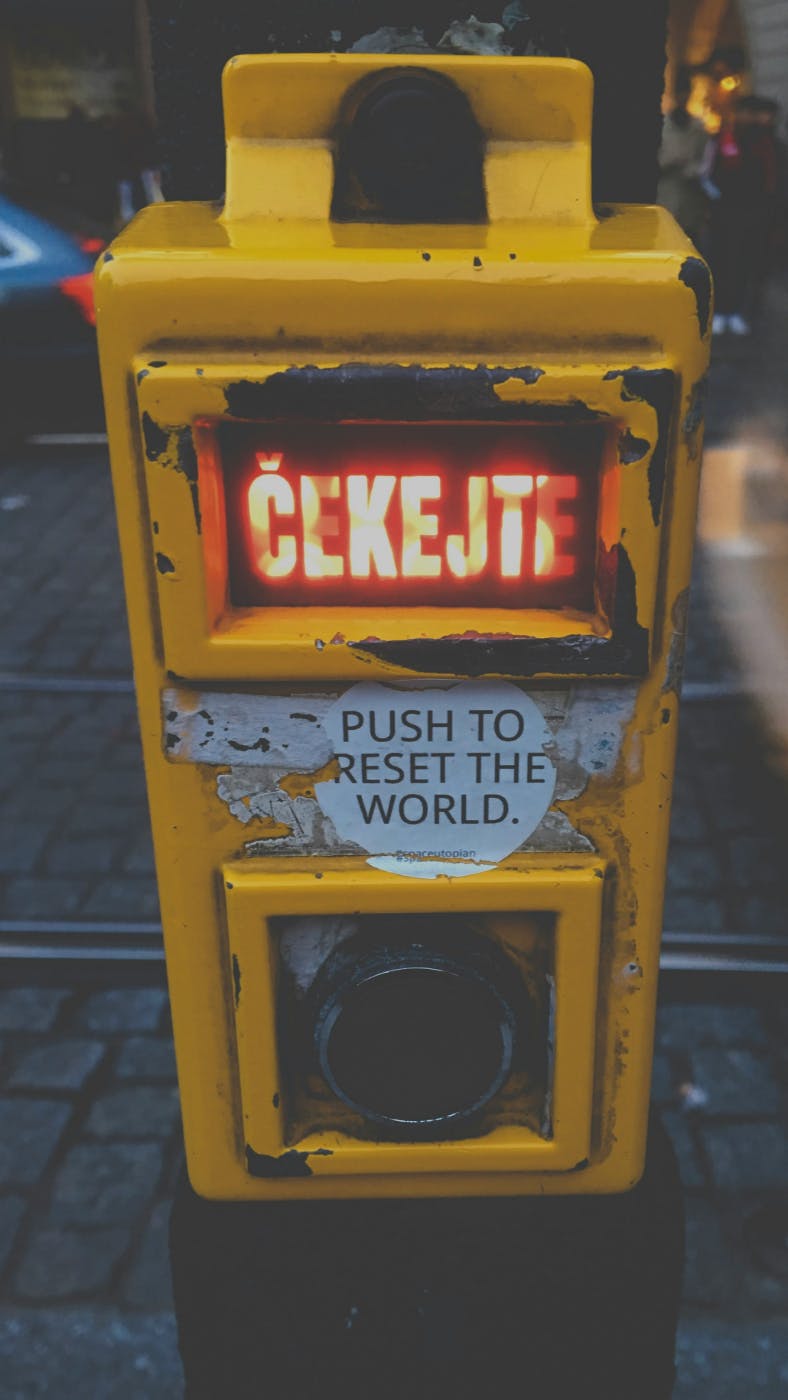 A yellow box with the word wait in Czech in red and a round sticker that reads; Push to reset the world
