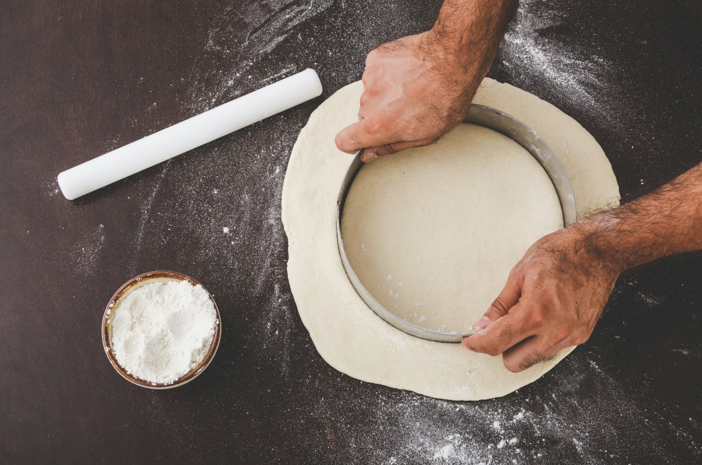 A person cutting a circle out of flattened dough