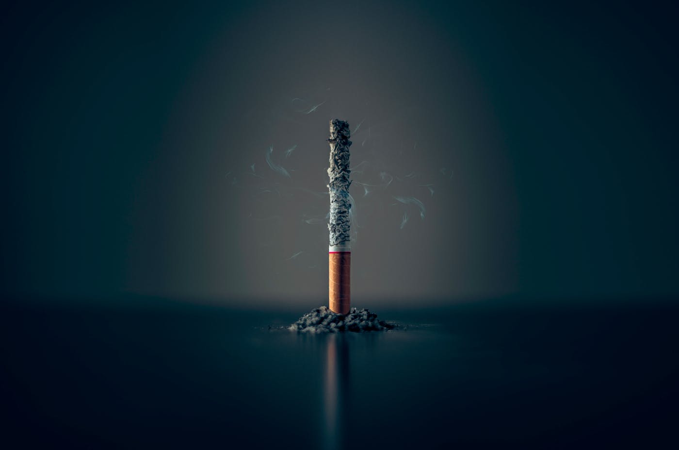 A cigarette. completely ash, standing on it's filtered end which is surrounded by ash