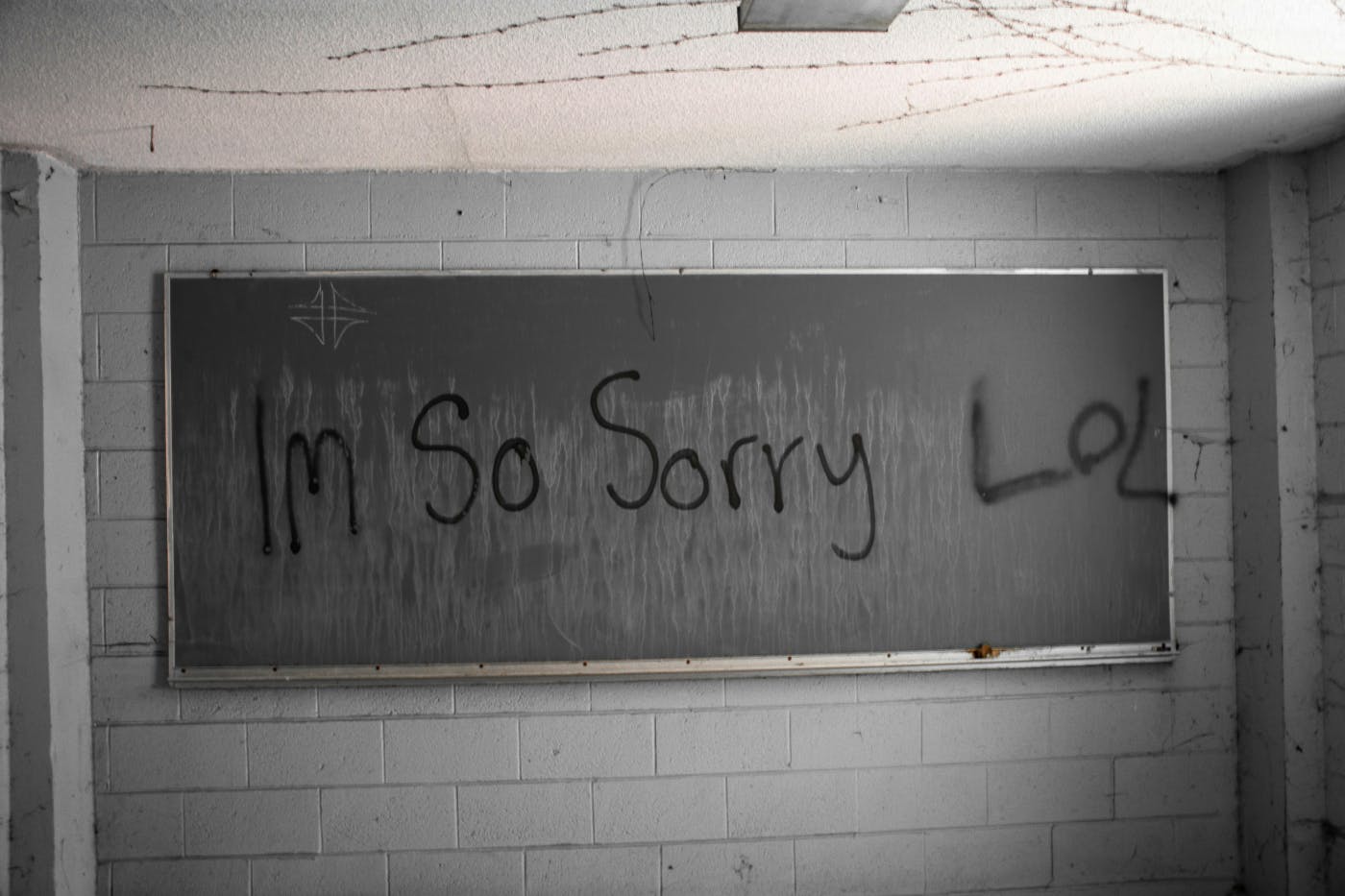 Graffiti on the chalkboard in an abandoned school room reading: I'm So Sorry