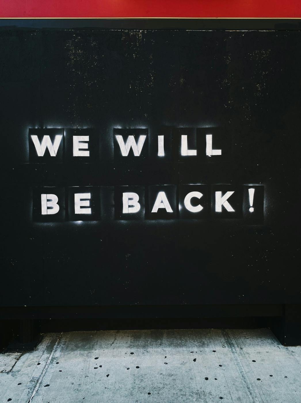 Stenciled white words on a black wall reading WE WILL BE BACK!