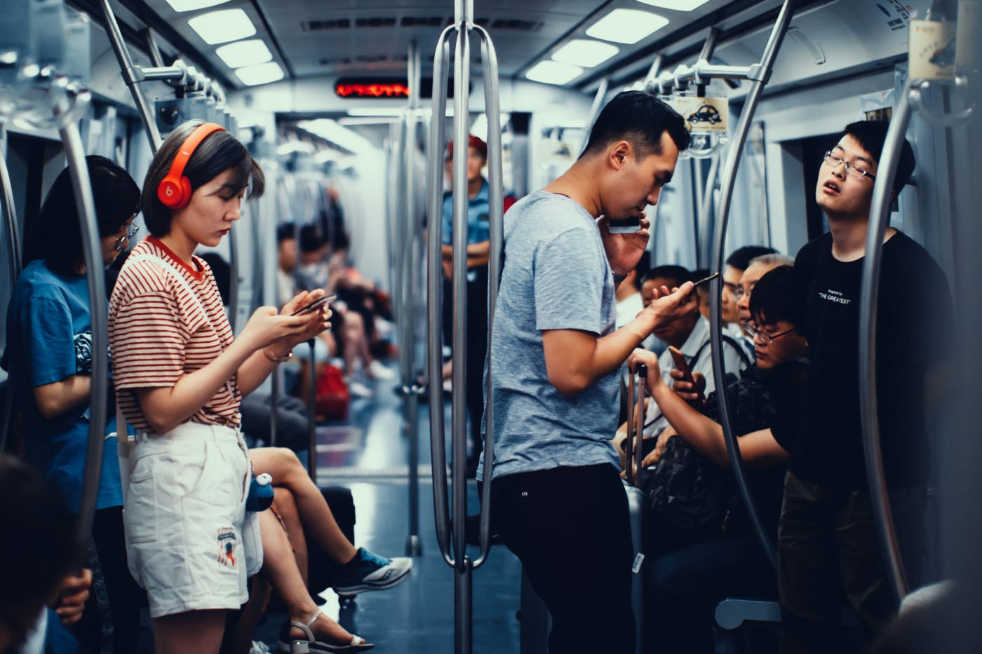 A subway car, everyone is on their phone except for one guy who's asleep standing up