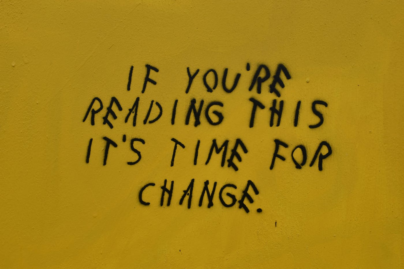 A mustard yellow wall with: If You're Reading This It's Time For Change in black letters
