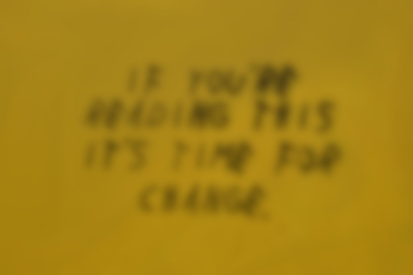 A mustard yellow wall with: If You're Reading This It's Time For Change in black letters