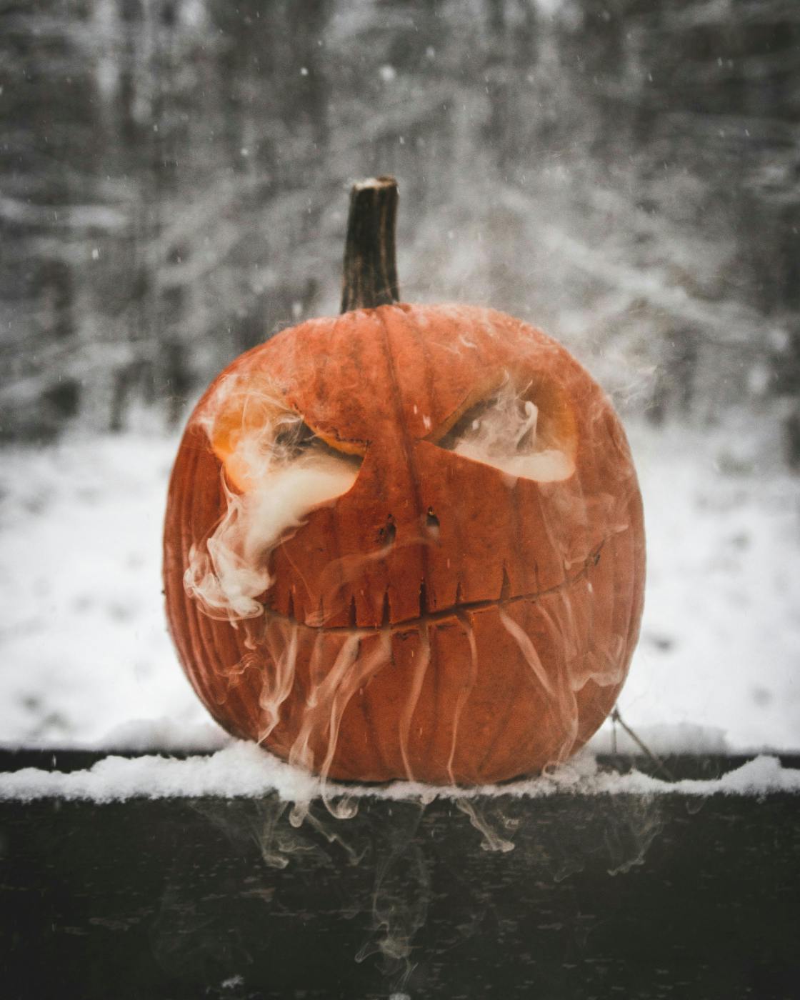 a carved pumpkin with smoke coming from its eyes and mouth against a snowy background
