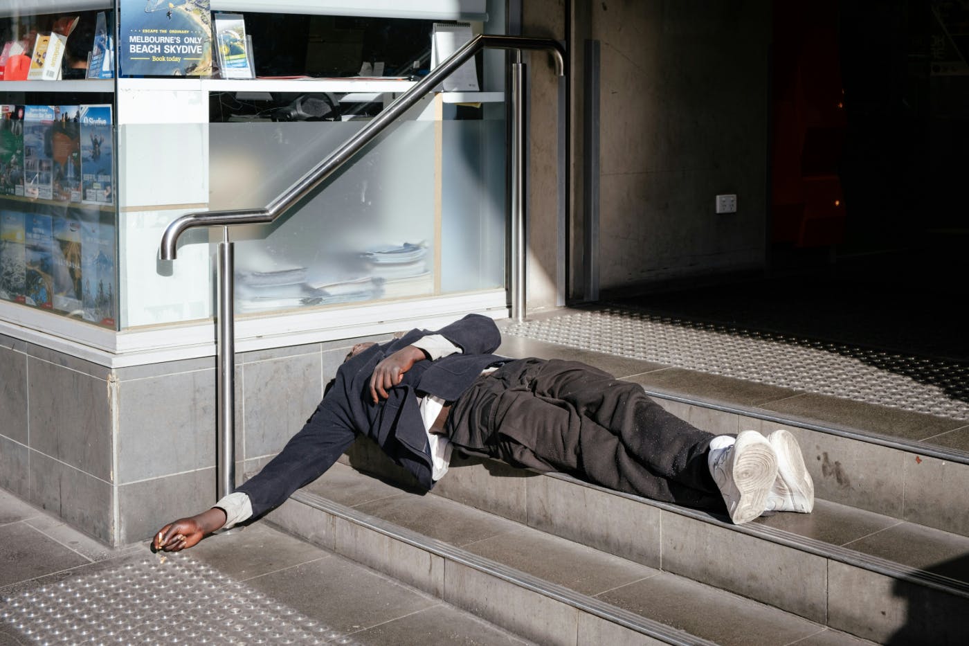 A man in a blue blazer and white shirt passed out on the stairs leading into a building