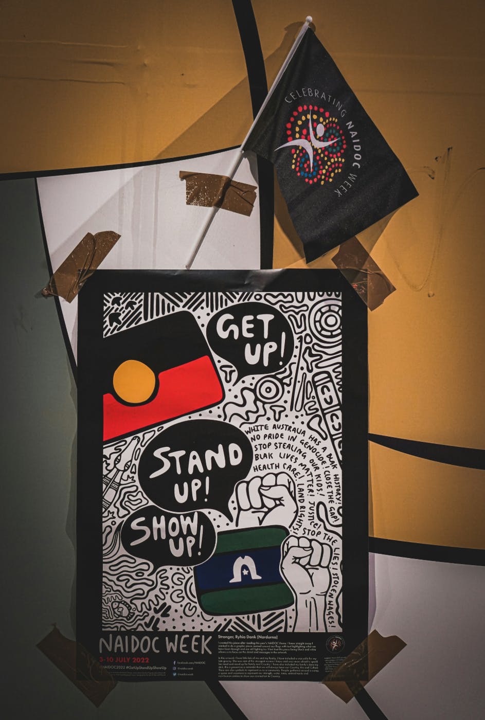 A poster taped to a wall reading Get Up, Stand Up, Show Up!