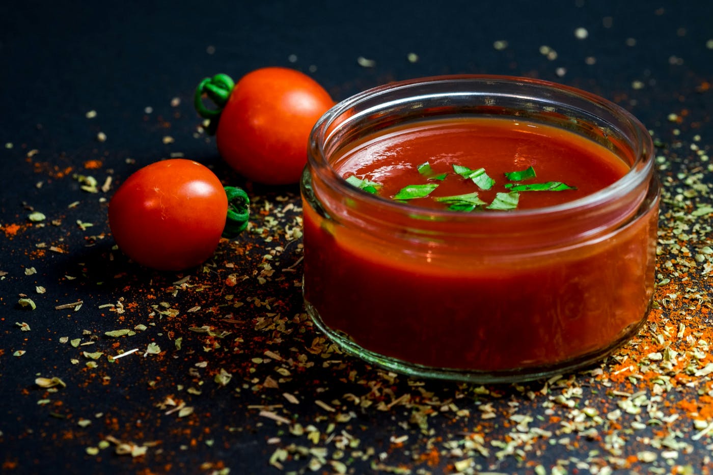 A low jar of red sauce with two cherry tomatoes beside it