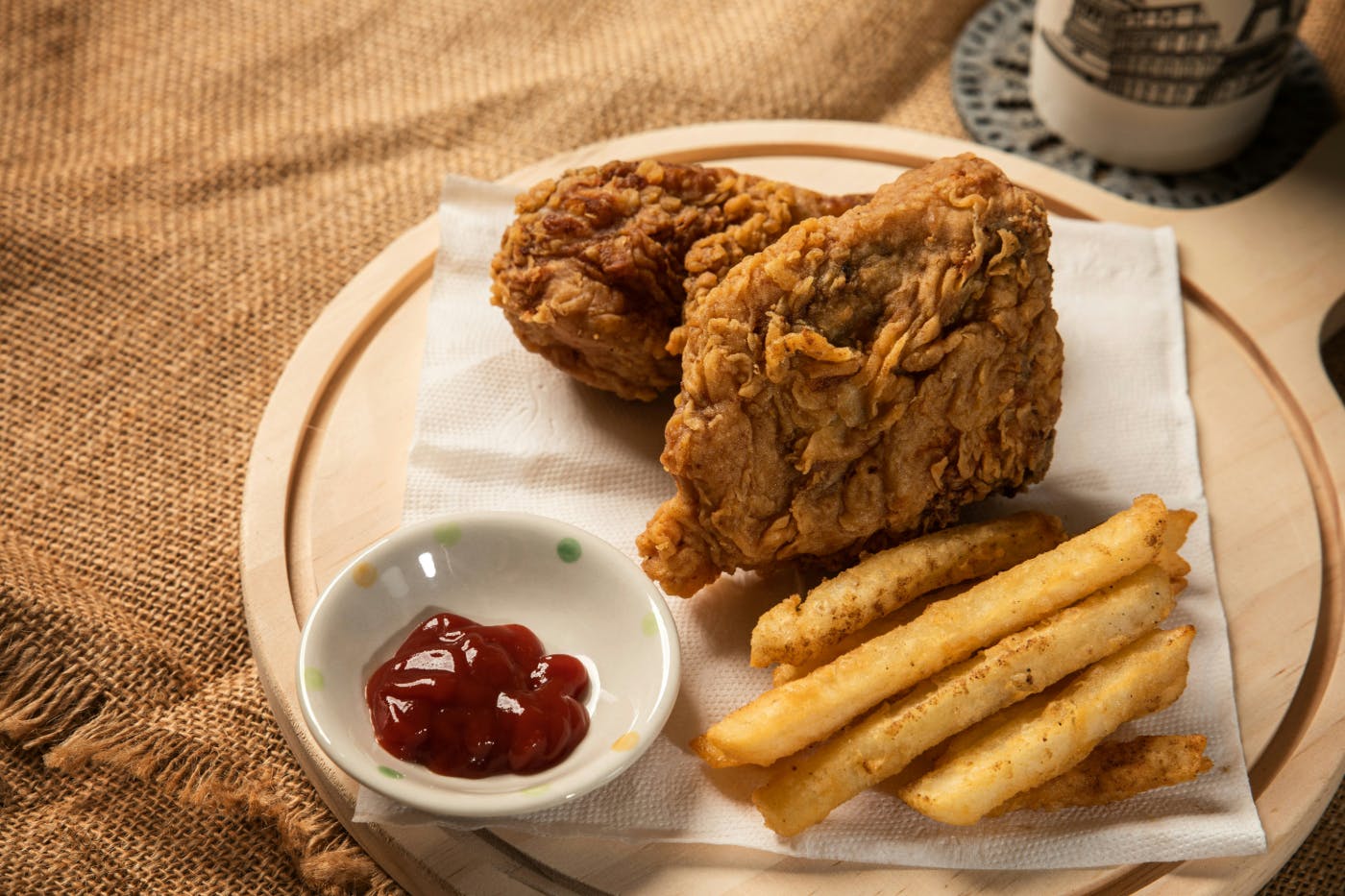 A wooden plate with fried chicken, French fries and a small bowl for ketchup