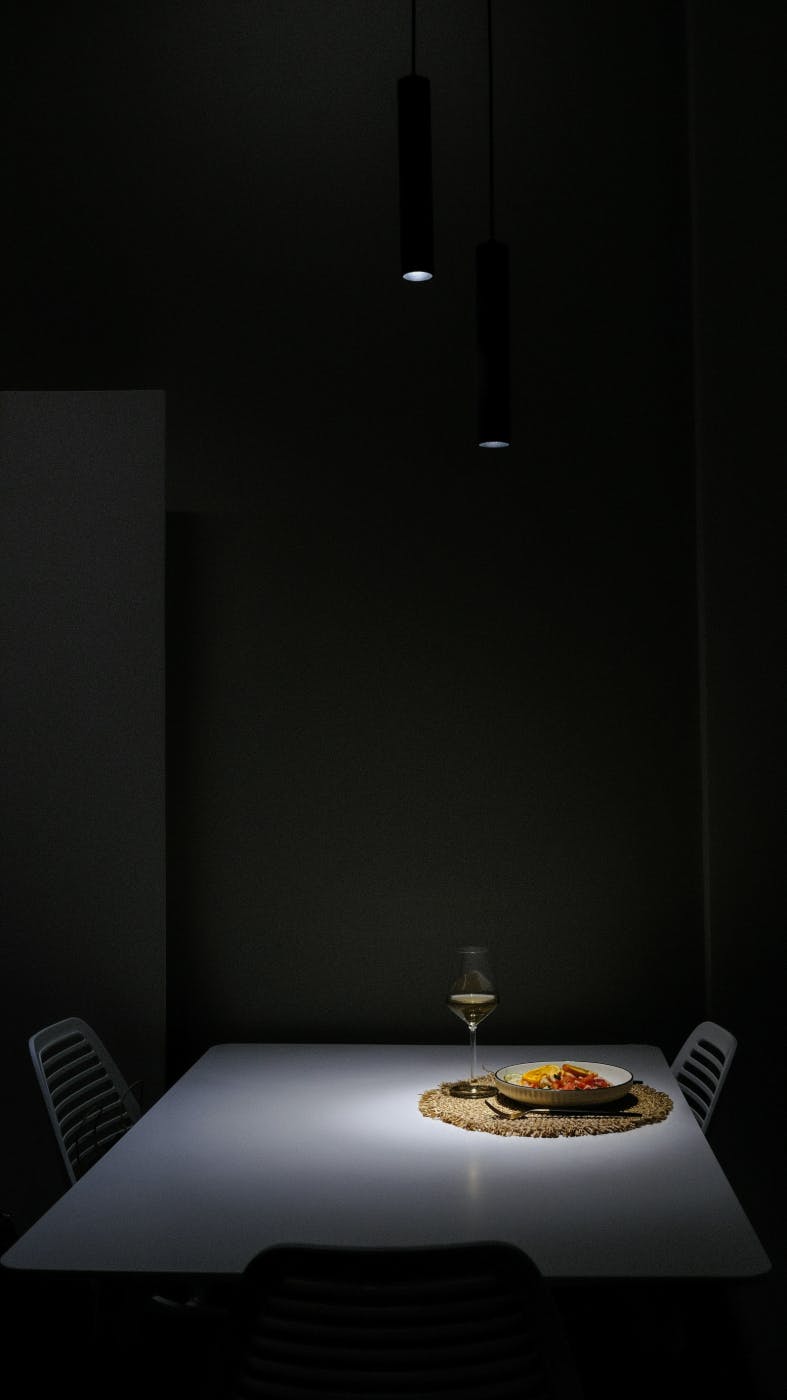 A dark room with downlights on a spare table with a setting for one