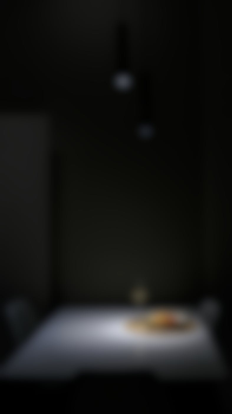 A dark room with downlights on a spare table with a setting for one