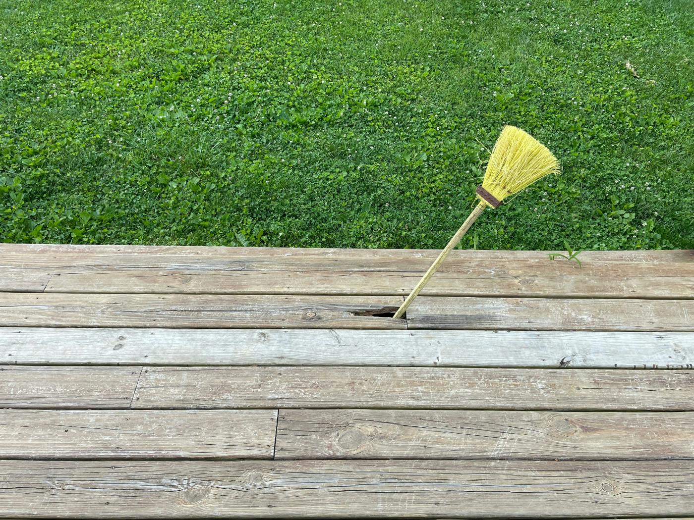 A broom sticking out of a hole in a wood deck
